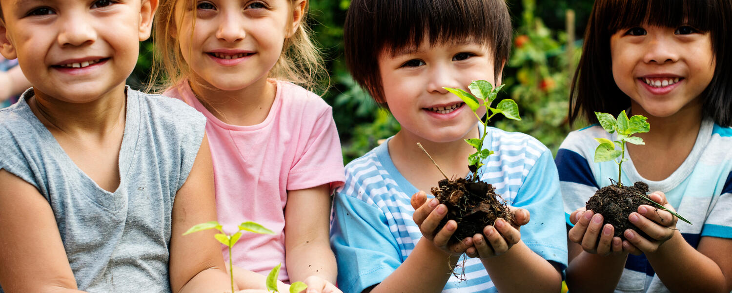 Four children smiling and holding small plants in their hands